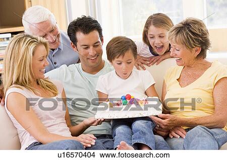 Picture - Family in living room smiling with young boy blowing out candles on cake. Fotosearch