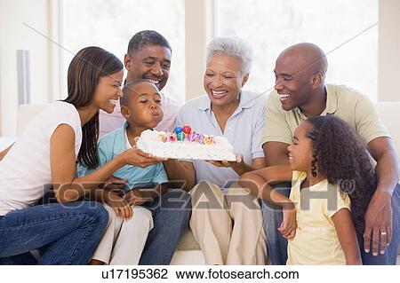 Stock Image - Family in living room smiling with young boy blowing out candles on cake. Fotosearch
