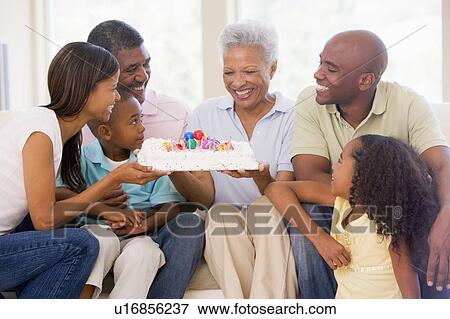 Stock Photo - Family in living room with cake smiling. Fotosearch