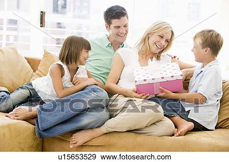 Family in living room with mother receiving gift and smiling View Large Photo Image Stock Photo - Family in living room with mother receiving gift and smiling. Fotosearch
