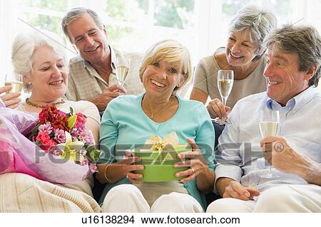 Picture - Five friends with champagne and gifts in living room smiling. Fotosearch