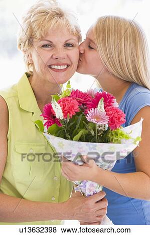 Stock Photo - Granddaughter kissing grandmother on cheek holding flowers and smiling. Fotosearch