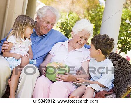 Stock Image - Grandparents with grandchildren on patio with gift smiling. Fotosearch