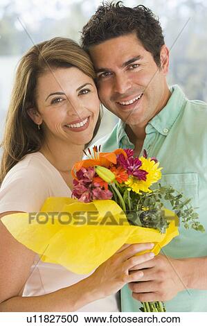 Stock Image - Husband and wife holding flowers and smiling. Fotosearch