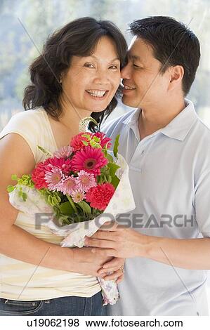 Stock Photo - Husband and wife holding flowers smiling. Fotosearch