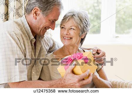 Husband giving wife gift in living room smiling View Large Photo Image Stock Photo - Husband giving wife gift in living room smiling. Fotosearch