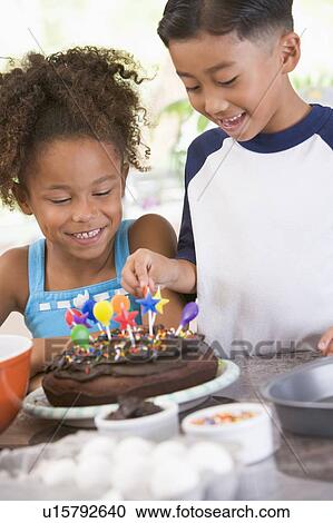 Stock Image - Two children in kitchen with birthday cake smiling. Fotosearch