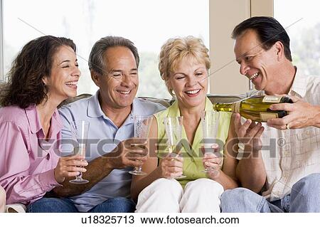 Stock Image - Two couples in living room drinking champagne and smiling. Fotosearch