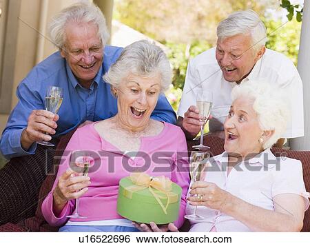 Stock Photograph - Two couples on patio with champagne and gift smiling. Fotosearch