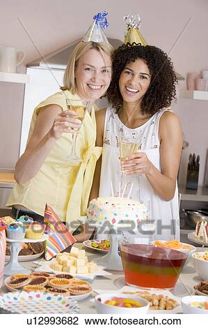 Two women at party holding drinks standing by food table smiling View Large Photo Image Stock Image - Two women at party holding drinks standing by food table smiling. Fotosearch