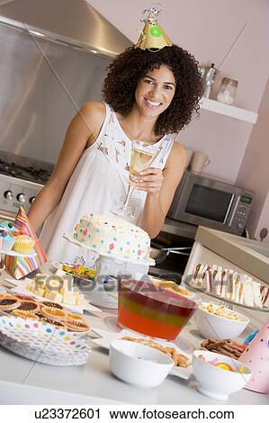 Stock Image - Woman at party holding drink standing by food table smiling. Fotosearch