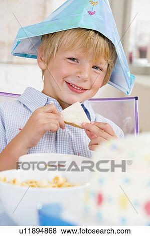 Young boy at party sitting at table with a sandwich smiling View Large Photo Image Stock Photo - Young boy at party sitting at table with a sandwich smiling. Fotosearch