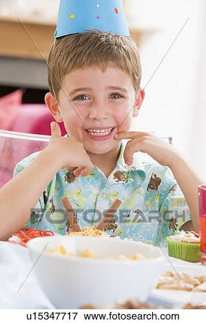 Young boy at party sitting at table with food smiling View Large Photo Image Stock Photo - Young boy at party sitting at table with food smiling. Fotosearch