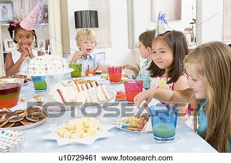 Stock Image - Young children at party sitting at table with food smiling. Fotosearch