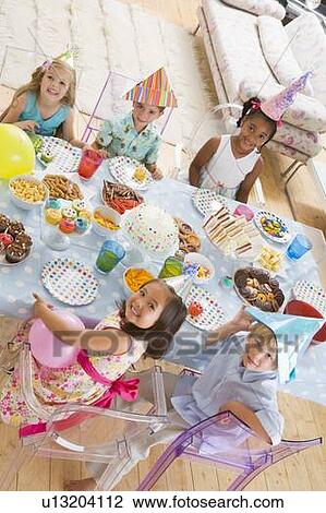 Young children at party sitting at table with food smiling View Large Photo Image Stock Image - Young children at party sitting at table with food smiling. Fotosearch