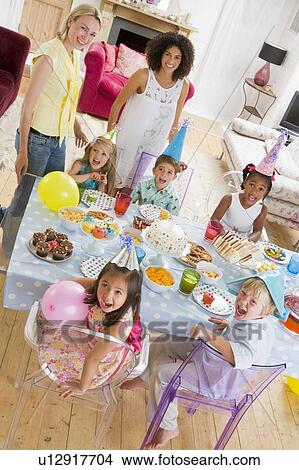 Picture - Young children at party with mothers sitting at table with food smiling. Fotosearch