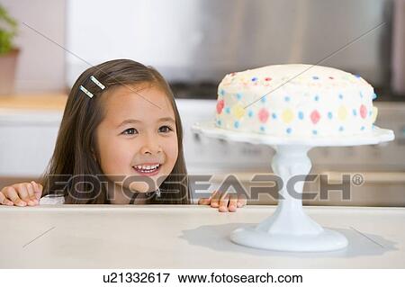 Young girl at kitchen counter looking at cake smiling View Large Photo Image Stock Photo - Young girl at kitchen counter looking at cake smiling. Fotosearch