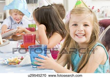 Stock Image - Young girl at party sitting at table with food smiling. Fotosearch