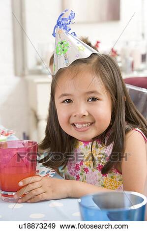 Young girl wearing party hat at table smiling View Large Photo Image Stock Photo - Young girl wearing party hat at table smiling. Fotosearch