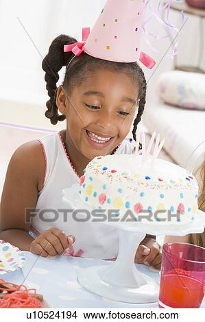 Young girl wearing party hat looking at cake smiling View Large Photo Image Picture - Young girl wearing party hat looking at cake smiling. Fotosearch