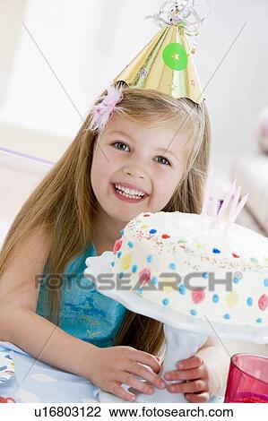 Stock Image - Young girl wearing party hat with birthday cake smiling. Fotosearch