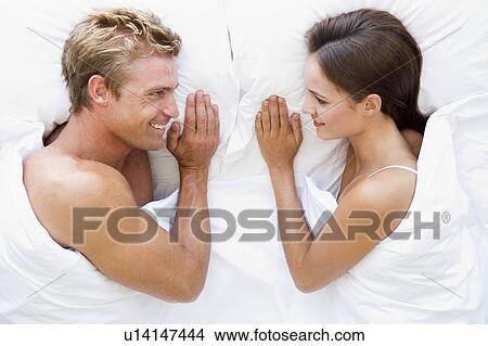 Picture - Couple lying in bed smiling. Fotosearch