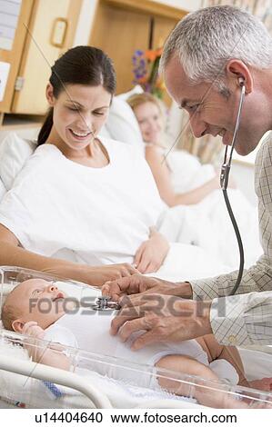 Stock Image - Doctor checking baby's heartbeat with new mother watching and smiling. Fotosearch