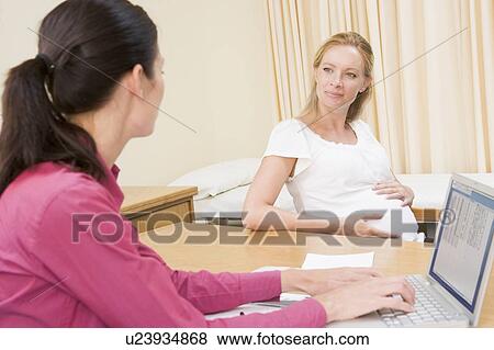 Stock Photo - Doctor with laptop and pregnant woman in doctor's office smiling. Fotosearch
