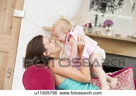 Stock Photograph - Pregnant mother in living room holding daughter and laughing. Fotosearch