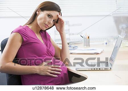 Stock Photo - Pregnant woman at work with laptop looking stressed. Fotosearch