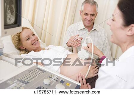 Stock Image - Pregnant woman getting ultrasound from doctor with husband watching. Fotosearch