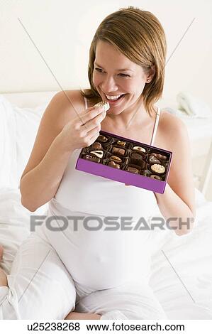 Pregnant woman in bed eating chocolate smiling View Large Photo Image Stock Photo - Pregnant woman in bed eating chocolate smiling. Fotosearch