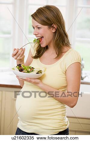 Pregnant woman in kitchen eating a salad smiling View Large Photo Image Stock Photography - Pregnant woman in kitchen eating a salad smiling. Fotosearch