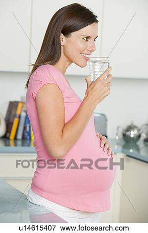 Stock Photo - Pregnant woman in kitchen with glass of water smiling. Fotosearch