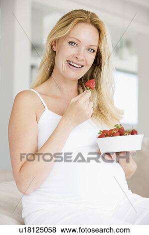 Stock Photo - Pregnant woman with bowl of strawberries smiling. Fotosearch