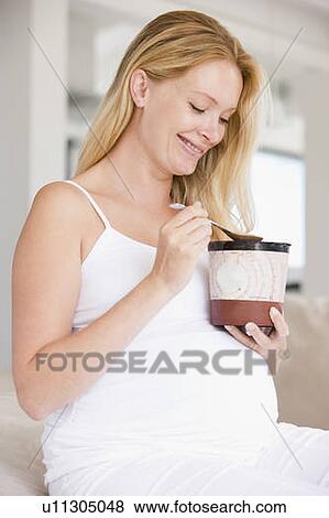 Stock Photo - Pregnant woman with bucket of ice cream smiling. Fotosearch