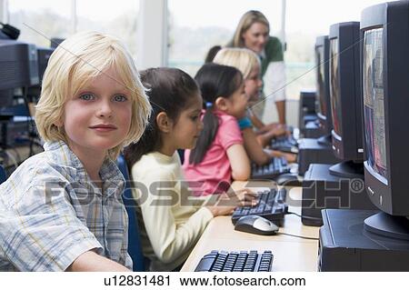 Stock Image - Children at computer terminals with teacher in background (depth of field/high key). Fotosearch