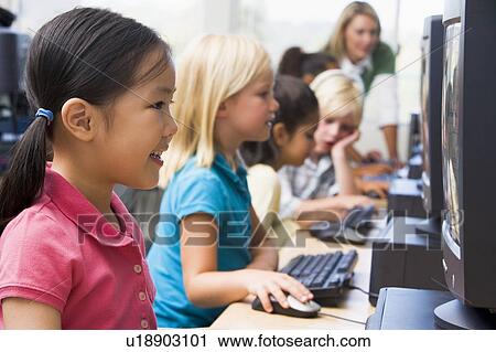 Stock Image - Children at computer terminals with teacher in background (depth of field/high key). Fotosearch