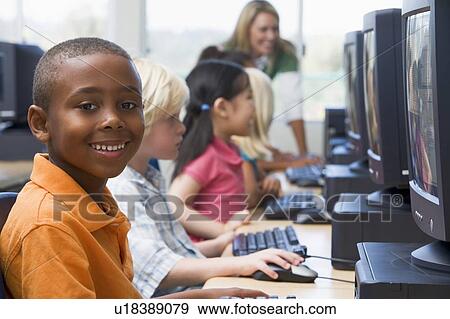 Stock Photo - Children at computer terminals with teacher in background (depth of field/high key). Fotosearch