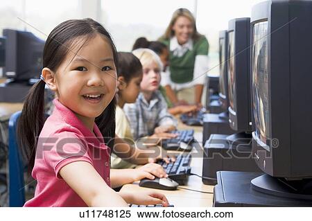 Stock Photography - Children at computer terminals with teacher in background (depth of field/high key). Fotosearch