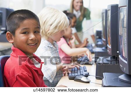 Stock Image - Four children at computer terminals with teacher in background (depth of field/high key). Fotosearch