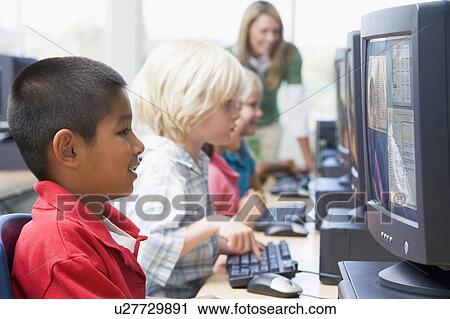 Stock Image - Four children at computer terminals with teacher in background (depth of field/high key). Fotosearch