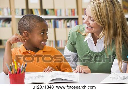Stock Photo - Student in class reading with teacher. Fotosearch