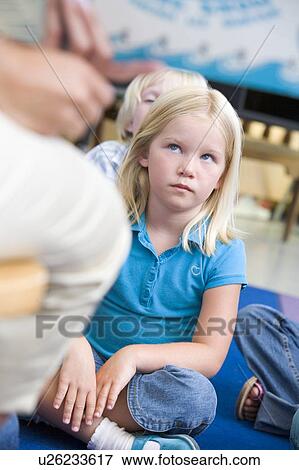 Stock Photo - Student in class sitting on floor looking at teacher (selective focus). Fotosearch