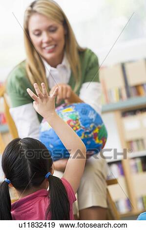 Teacher in class showing a globe with student volunteering in foreground (selective focus) View Large Photo Image Stock Photo - Teacher in class showing a globe with student volunteering in foreground (selective focus). Fotosearch