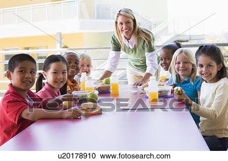 Stock Image - Teacher leaning on table outdoors while students eat lunch (high key). Fotosearch