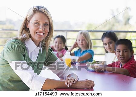 Teacher sitting at table outdoors with students eating lunch in background (depth of field) View Large Photo Image Stock Photo - Teacher sitting at table outdoors with students eating lunch in background (depth of field). Fotosearch