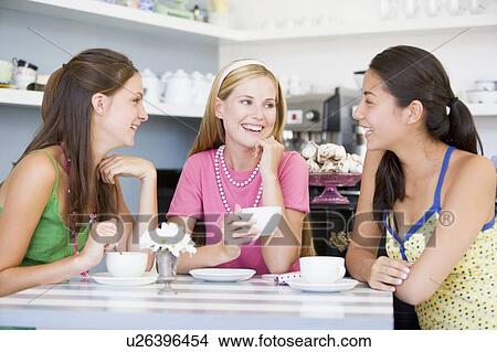 Three young woman sitting at a table and drinking tea View Large Photo Image Picture - Three young woman sitting at a table and drinking tea. Fotosearch