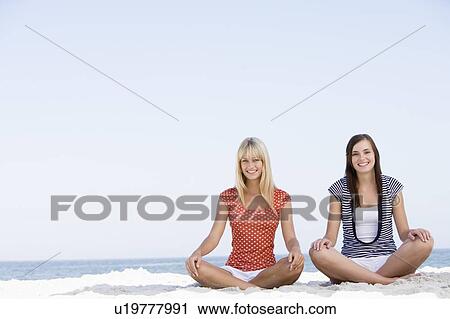 Stock Image - Two women sitting and meditating on a beach. Fotosearch