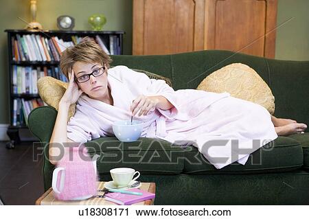 Young woman lying on sofa at home eating a sweet treat View Large Photo Image Stock Image - Young woman lying on sofa at home eating a sweet treat. Fotosearch